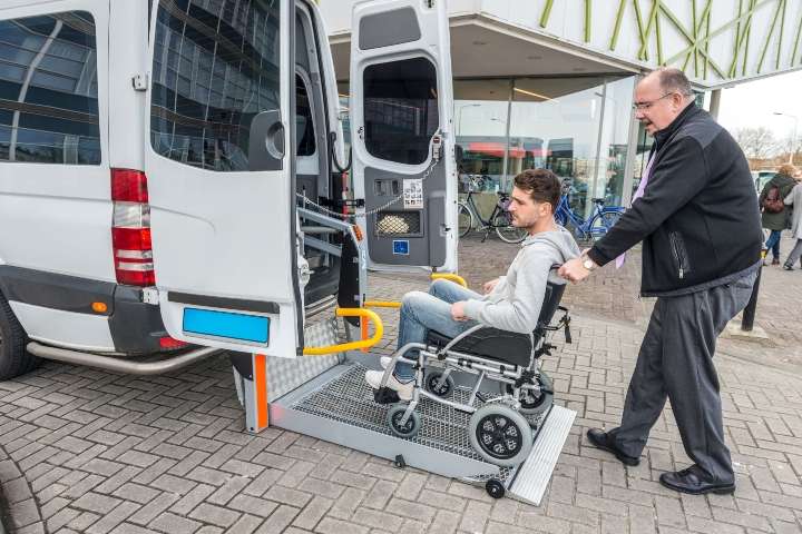 An attendant helping a wheelchair user board an accessible paratransit van